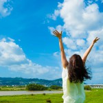 青空に向かって手を広げる一人の女性